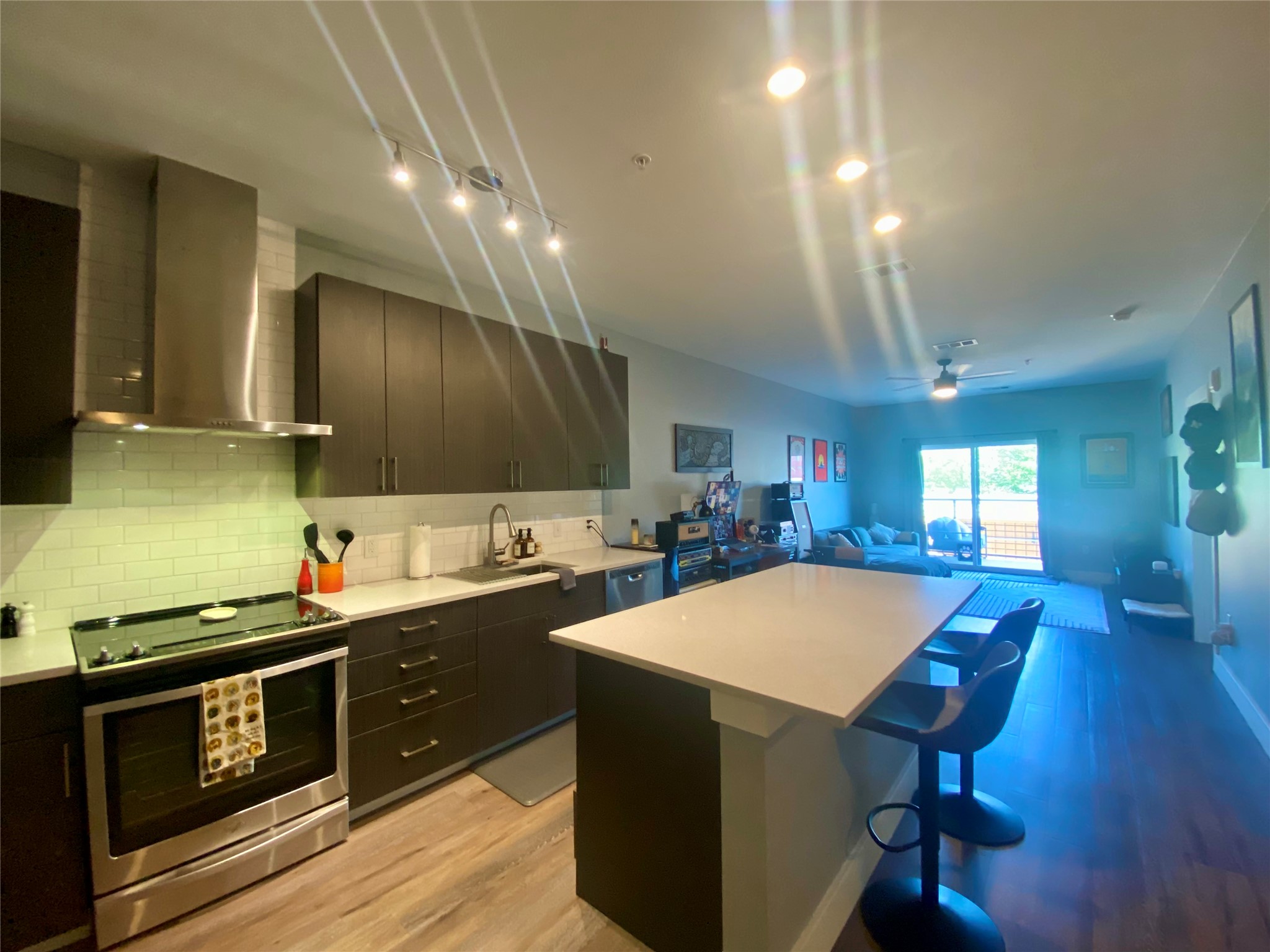 6444 Burnet Road, Unit 203 Austin, TX 78757 - Photo 25 of 30 Open concept kitchen featuring dark cabinetry, stainless steel appliances, and a light-colored island with seating, leading into a living area with a sliding glass door