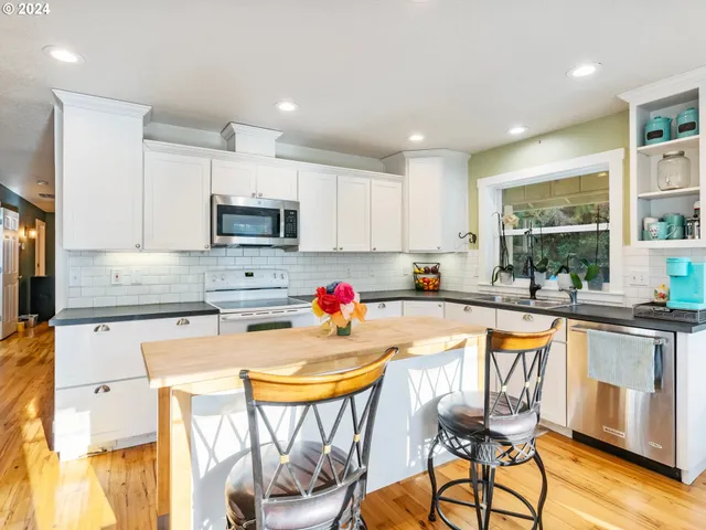 a kitchen with stainless steel appliances granite countertop a stove top oven a sink a refrigerator and chairs