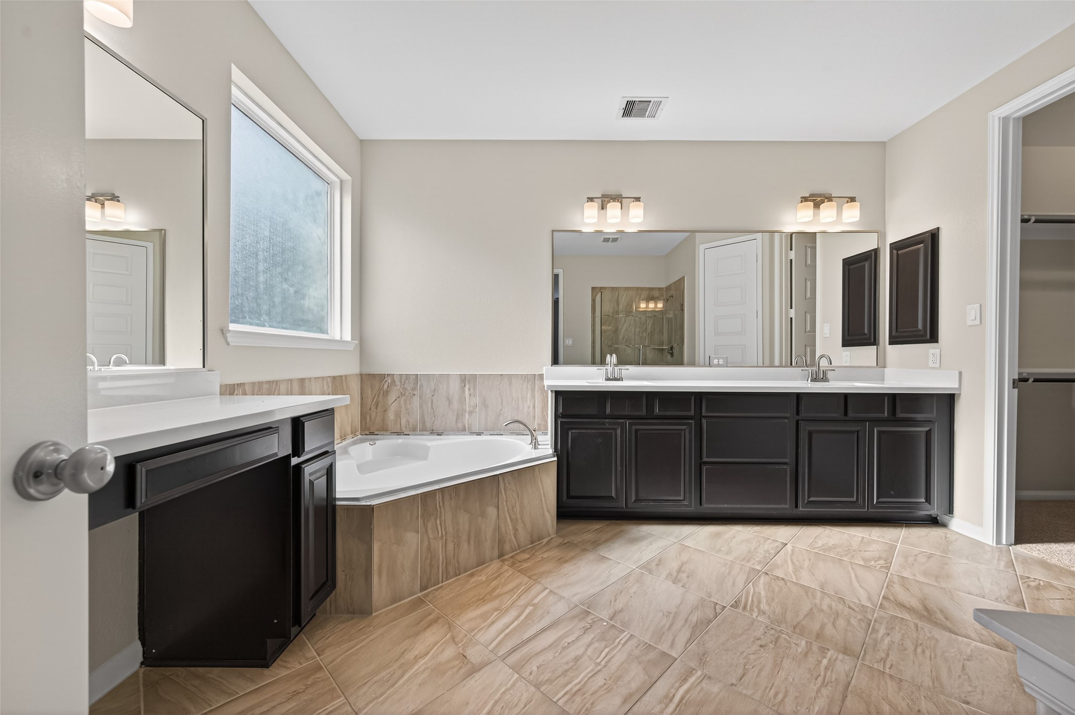 7003 Bristol Memorial Drive Spring, TX 77379 - Photo 22 of 40 Spacious primary bathroom in this Spring TX 77379 home featuring dual vanities with extended counter space, framed mirrors, and updated lighting. A large soaking tub with tile surround creates a relaxing focal point, while neutral finishes and tile flooring provide a clean, modern look. The open layout offers functional separation between bathing and vanity areas, enhancing everyday convenience. Located within the private primary suite, this well-appointed bath complements the home’s generous layout