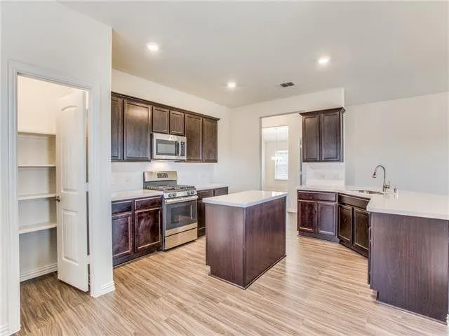 a large kitchen with stainless steel appliances granite countertop a stove top oven a refrigerator a sink dishwasher with wooden cabinets and floor