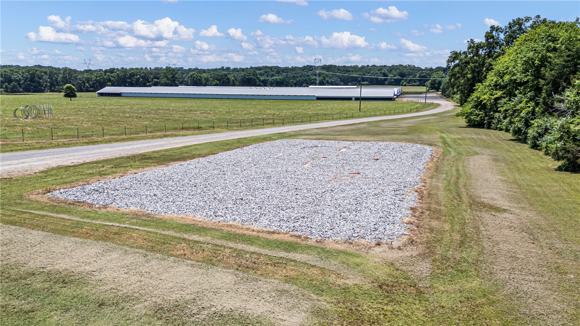 276 Charton Road Morrilton, AR 72110 - Photo 32 of 37 Expansive gravel pad with a paved drive, surrounded by grass and distant agricultural buildings