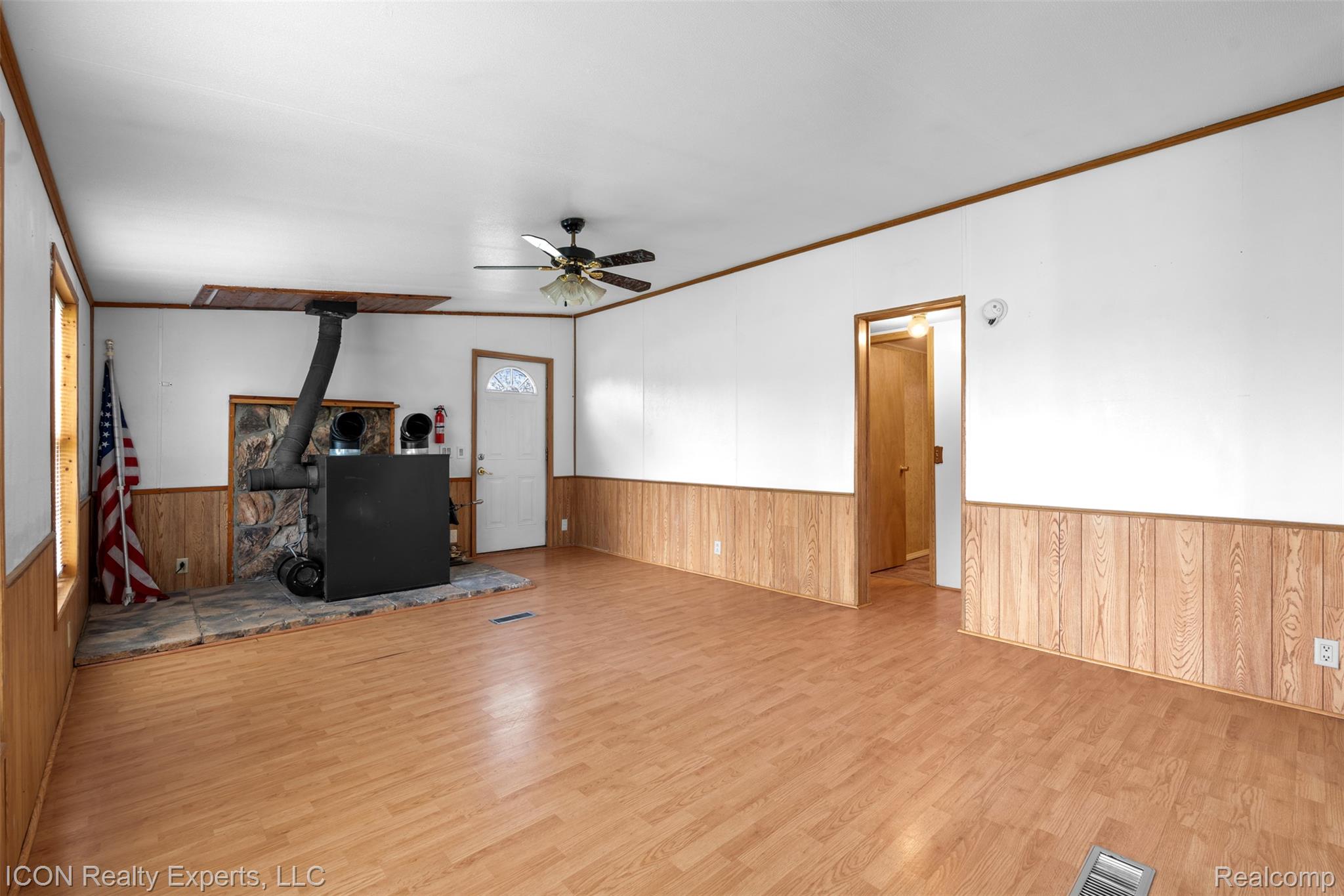 13620 Gilbert Road Allenton, MI 48002 - Photo 14 of 47 Unfurnished living room with wooden walls, a ceiling fan, wainscoting, ornamental molding, and a wood stove