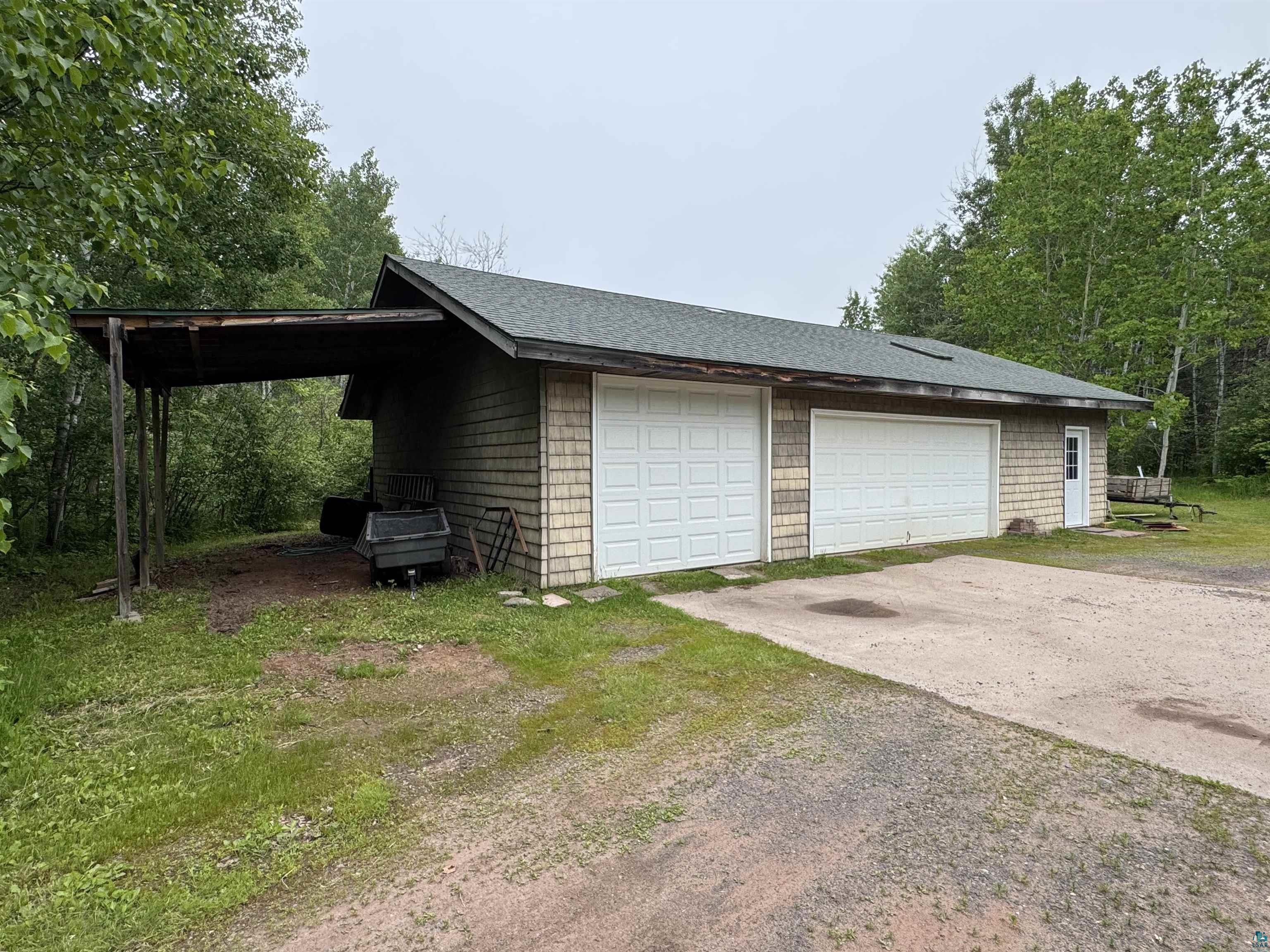 1745 Becks Road Maple, WI 54854 - Photo 42 of 46 four-car garage with shaker-style siding, a dark shingle roof, and a gravel and concrete driveway