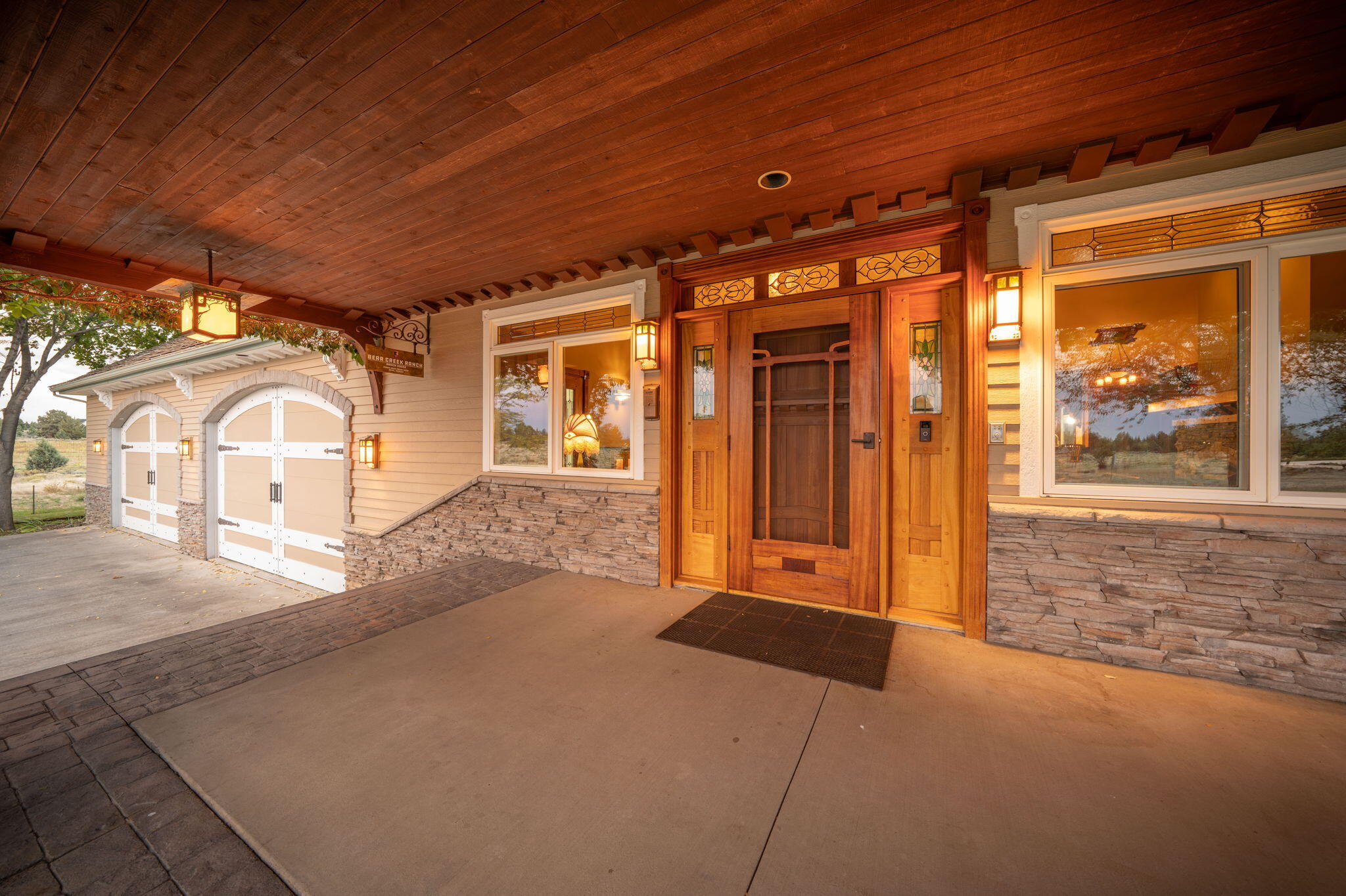 21925 Bear Creek Road Bend, OR 97702 - Photo 5 of 104 Front entryway door is Brazilian cherry w/African mahogany screen doors in the Green & Green style. Handmade stained glass and copper light fixtures at night. Large concrete covered porch and 4-car garage w/doors made to look like barn doors