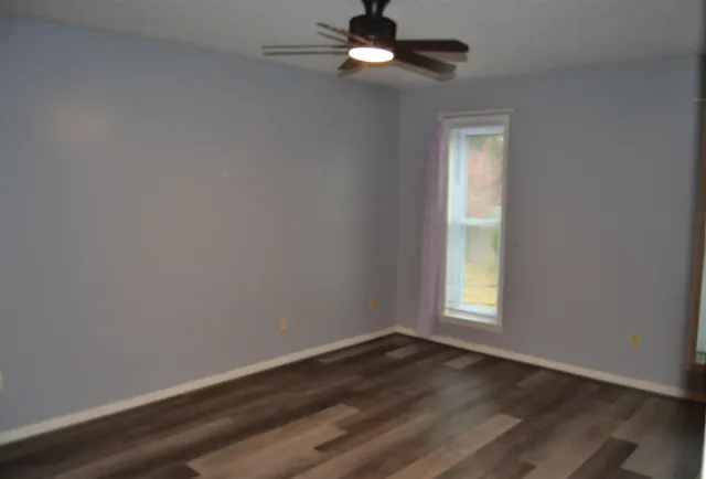 an empty room with wooden floor fan and windows