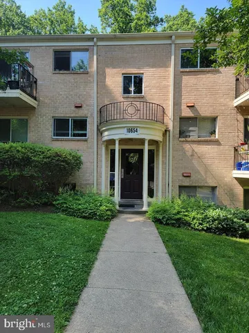 a view of a white house with a small yard plants and large tree