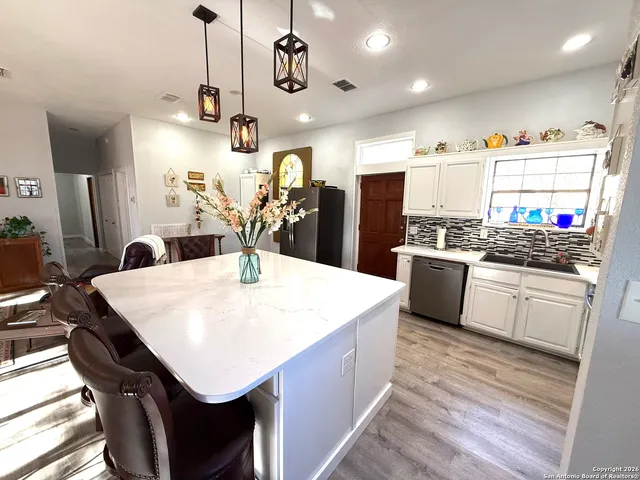 a kitchen with stainless steel appliances kitchen island granite countertop a refrigerator a stove top oven a sink dishwasher and white cabinets with wooden floor