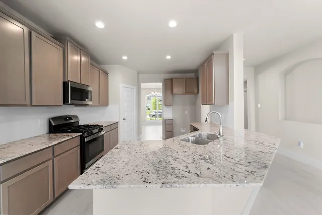 a kitchen with granite countertop stainless steel appliances a sink a stove top oven a counter space and cabinets