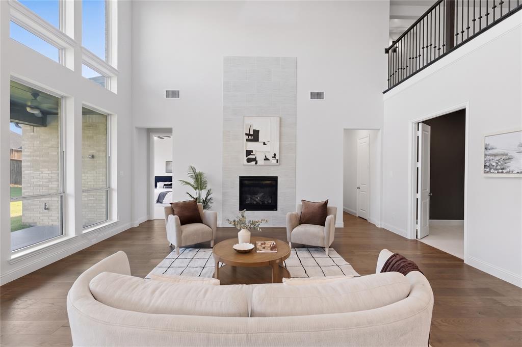 1316 Limestone Ridge Road Mansfield, TX 76063 - Photo 11 of 40 Two-story living area featuring a fireplace with a tile surround, wood-finish flooring, a wrought iron balcony, and expansive window walls