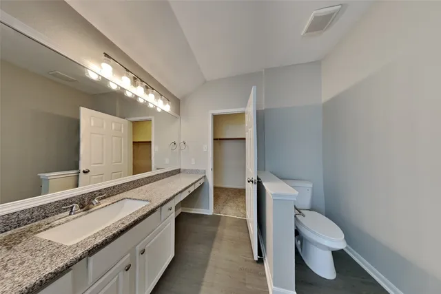 a bathroom with a granite countertop double vanity sink a mirror and a toilet