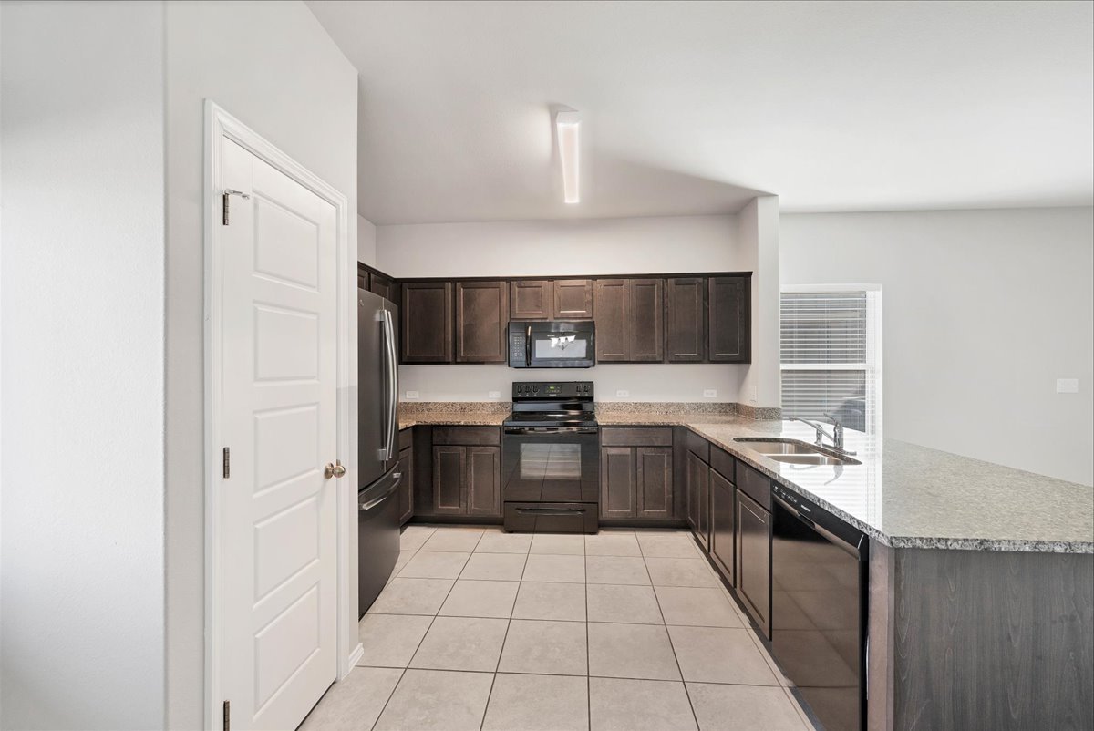 1202 Garland Road Georgetown, TX 78626 - Photo 12 of 28 Kitchen featuring dark wood-finish cabinetry, light-toned granite countertops, and black appliances