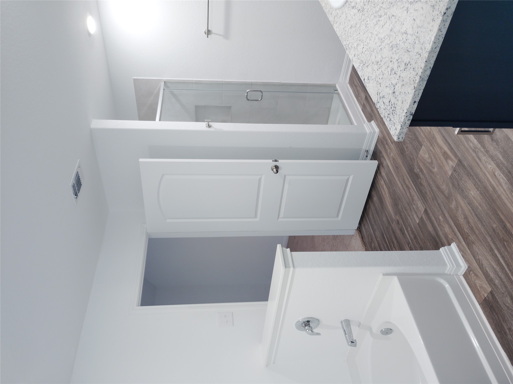 14024 Prairie Schooner Pass Elgin, TX 78621 - Photo 10 of 20 Bathroom featuring wood-finish flooring, a white bathtub with a chrome faucet, a separate glass-enclosed shower, and a vanity with a speckled countertop and dark cabinetry