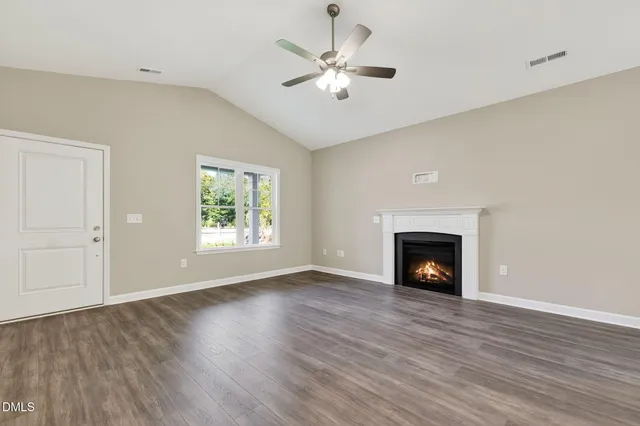 an empty room with windows a fireplace a ceiling fan and wooden floor