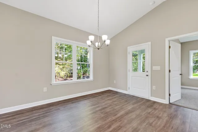 an empty room with wooden floor chandelier and windows