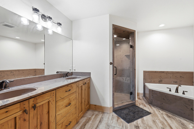 306 Spring Road Preston, ID 83263 - Photo 17 of 55 Bathroom featuring a double vanity with wood-finish cabinetry and light-toned countertops, a glass-enclosed shower with a wood-trimmed frame, a built-in tub with dark-toned surround, and wood-finish tile flooring