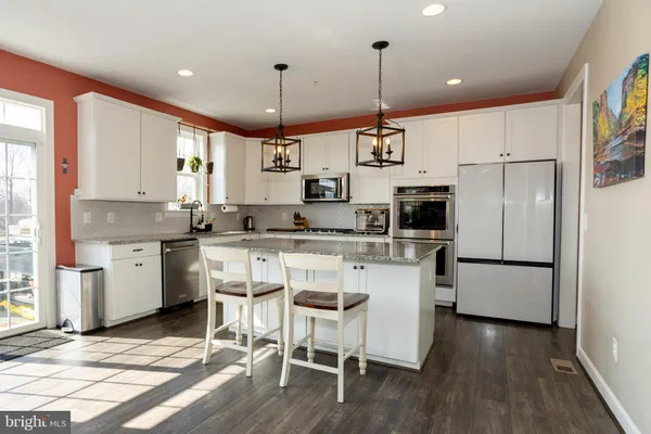 a kitchen with stainless steel appliances granite countertop a refrigerator a sink dishwasher a stove and white cabinets with wooden floor