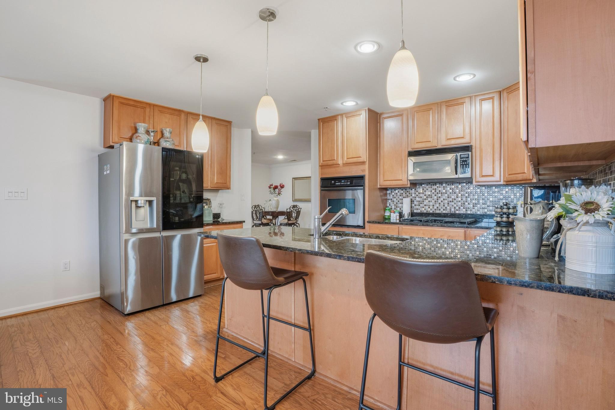9500 Sidebrook Road, Unit 406 Owings Mills, MD 21117 - Photo 14 of 35 a kitchen with stainless steel appliances granite countertop a refrigerator a sink a stove a dining table and chairs with wooden floor