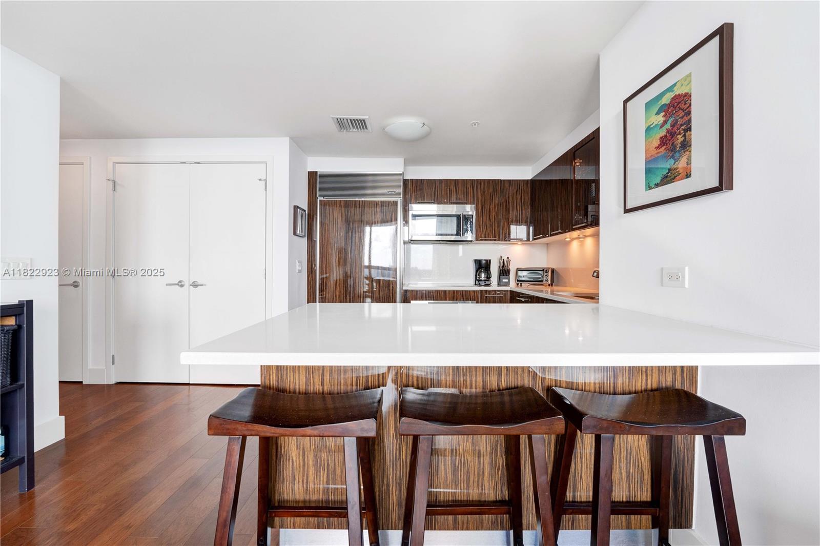 6899 Collins Avenue, Unit 1409 Miami Beach, FL 33141 - Photo 27 of 35 a kitchen with granite countertop a refrigerator and wooden floor