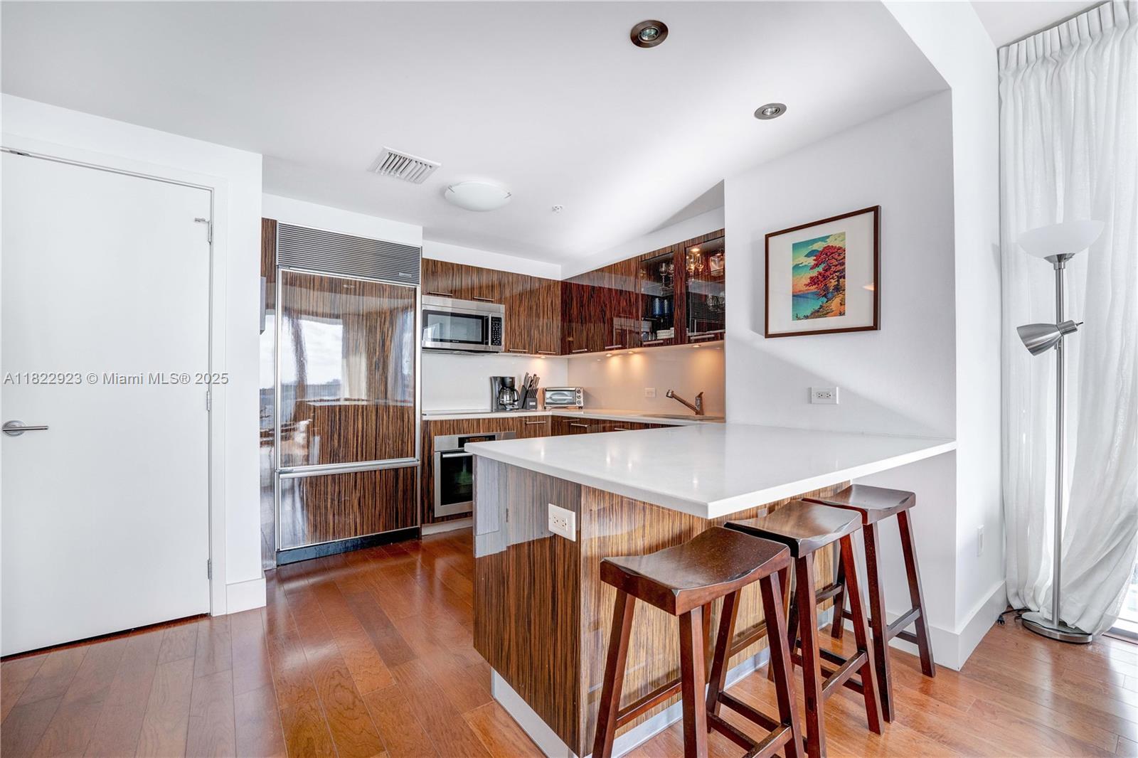 6899 Collins Avenue, Unit 1409 Miami Beach, FL 33141 - Photo 8 of 35 a room with stainless steel appliances kitchen island granite countertop a refrigerator a stove top oven a sink dishwasher and white cabinets with wooden floor