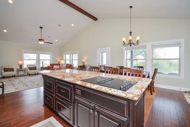 a kitchen with granite countertop a stove a sink a dining table and chairs with wooden floor