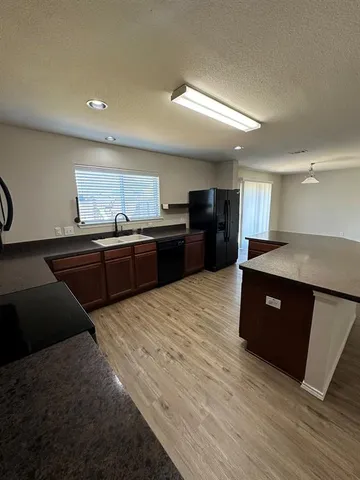 a large kitchen with stainless steel appliances granite countertop a refrigerator a sink dishwasher and a black countertops with wooden floor