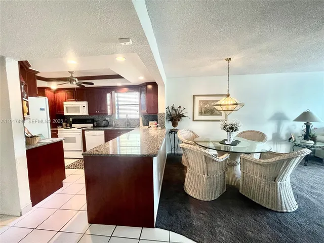 a living room with stainless steel appliances kitchen island granite countertop a table chairs and a wooden floors