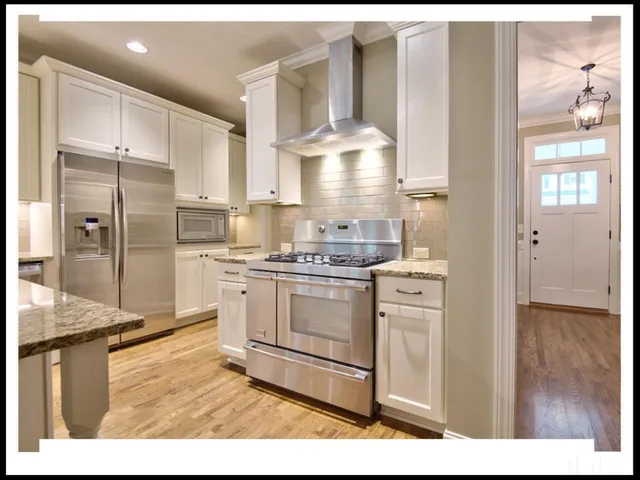 a kitchen with stainless steel appliances kitchen island granite countertop a refrigerator a sink and white cabinets