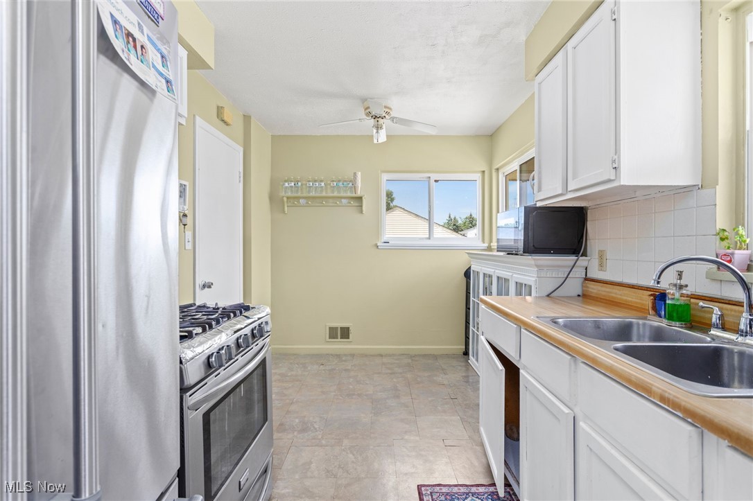 Kitchen with appliances with stainless steel finishes, decorative backsplash, white cabinetry, and ceiling fan