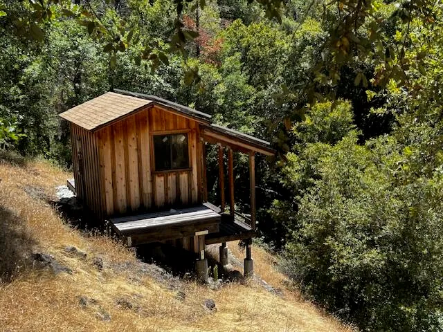 a wooden house with outdoor seating and trees in the background