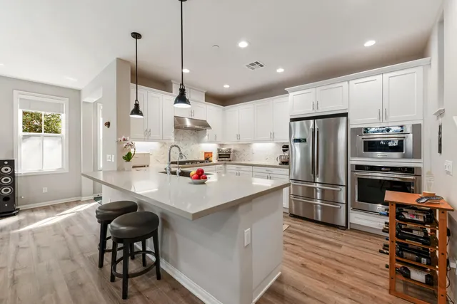 a kitchen with stainless steel appliances a table chairs refrigerator and wooden floor