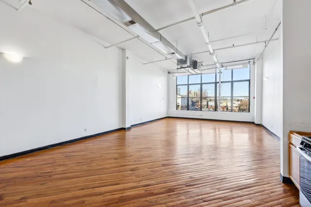a view of an empty room with window and wooden floor