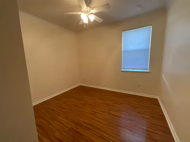 a view of an empty room with wooden floor and a chandelier fan