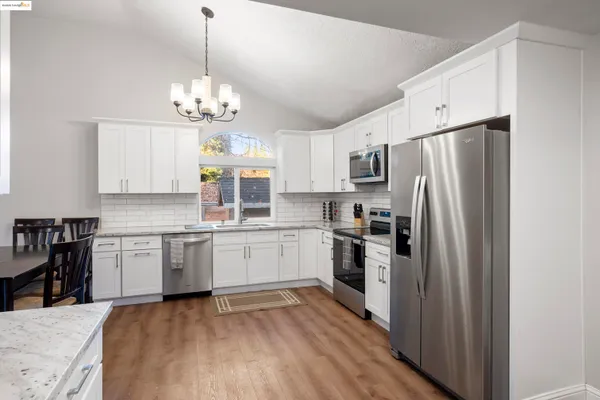 a kitchen with stainless steel appliances granite countertop a refrigerator a sink dishwasher a stove and white cabinets with wooden floor