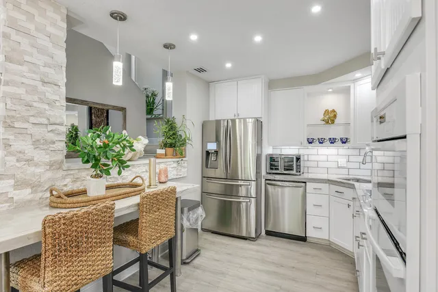 a kitchen with stainless steel appliances a refrigerator a stove a sink dishwasher and white cabinets with wooden floor