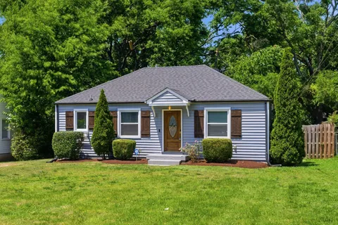 a view of a house with a yard plants and a large tree