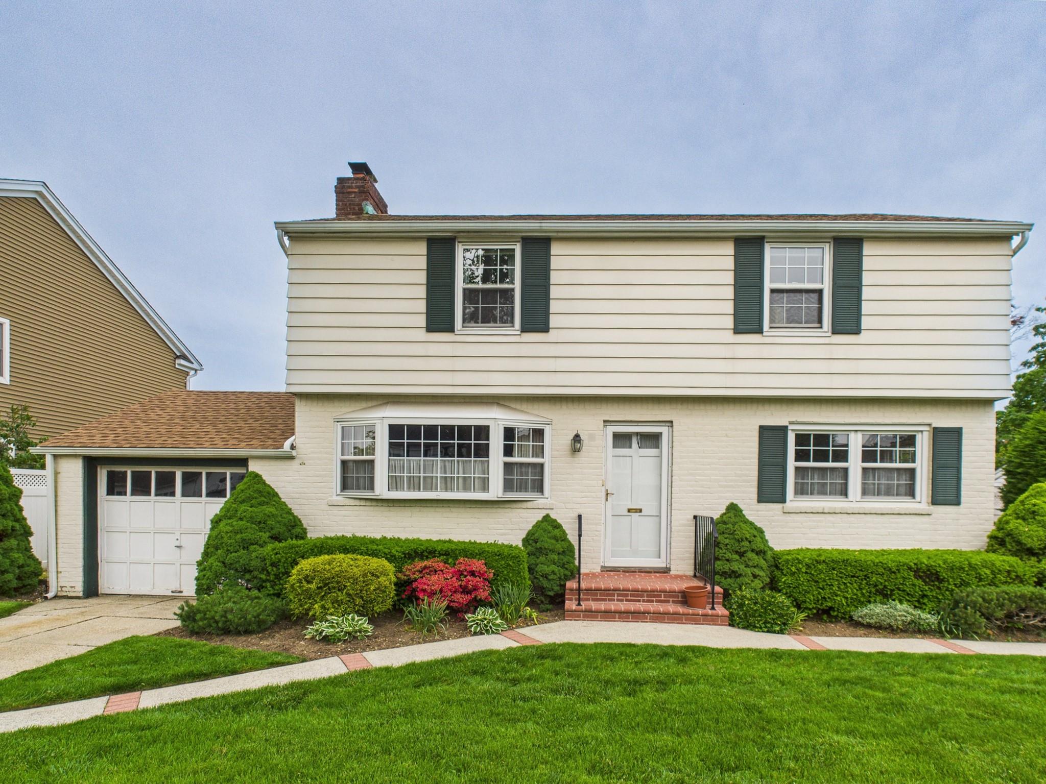 Colonial house featuring a chimney, a front lawn, an attached garage, driveway, and brick siding