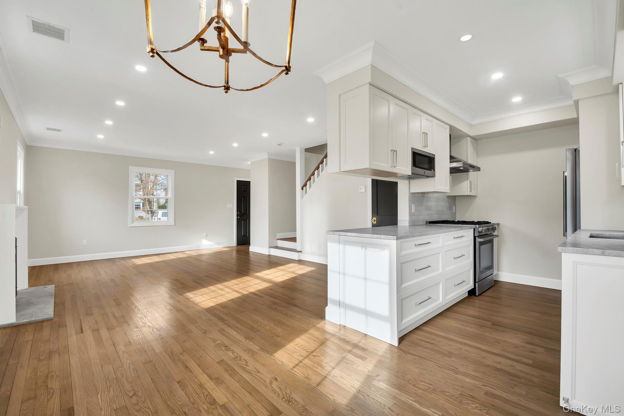 2 Bayview Court Manhasset, NY 11030 - Photo 5 of 21 Open Kitchen featuring white cabinetry, appliances with stainless steel finishes, dark wood-style floors, a chandelier, and ornamental molding
