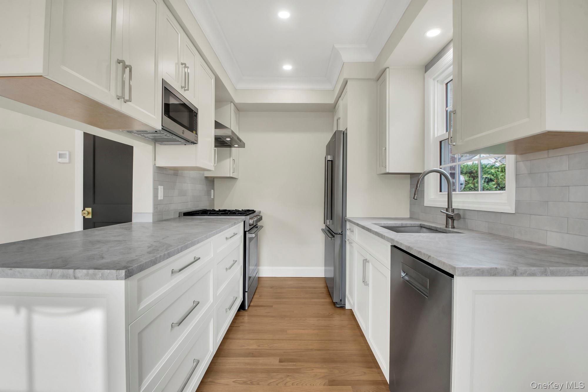 2 Bayview Court Manhasset, NY 11030 - Photo 8 of 21 Renovated Kitchen featuring appliances with stainless steel finishes, white cabinetry, tasteful backsplash, extractor fan, and light wood-style flooring