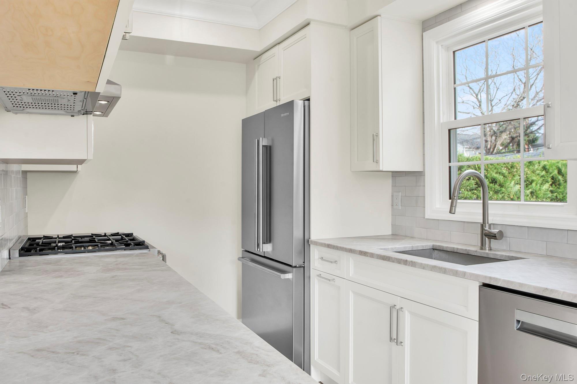 2 Bayview Court Manhasset, NY 11030 - Photo 9 of 21 Renovated Kitchen with white cabinets, stainless steel appliances, light stone countertops, decorative backsplash, and extractor fan