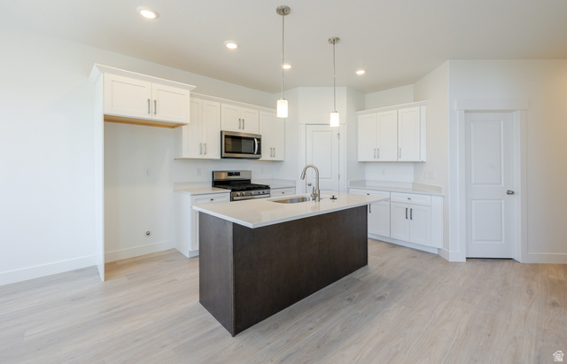 4720 Heartwood Road, Unit 438 Mapleton, UT 84664 - Photo 9 of 19 Kitchen featuring stainless steel appliances, an island with sink, light wood-style flooring, two tone color scheme, and decorative light fixtures