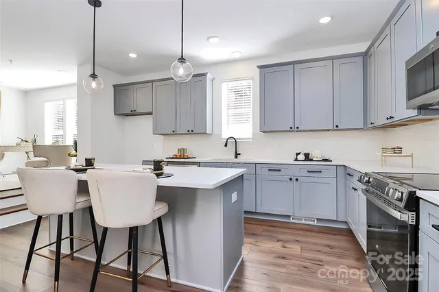 a large white kitchen with a large island oven a sink dishwasher and a large refrigerator with wooden floor