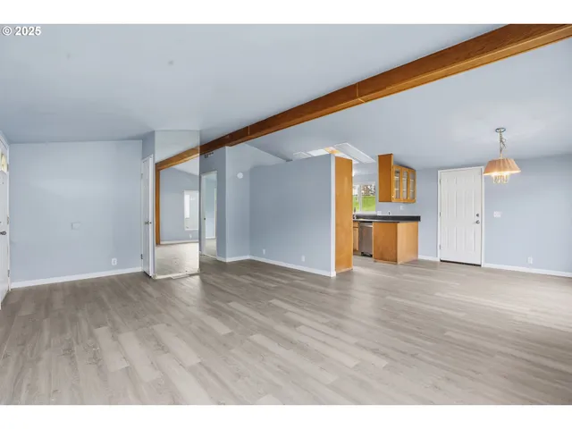 a view of empty room with wooden floor and kitchen