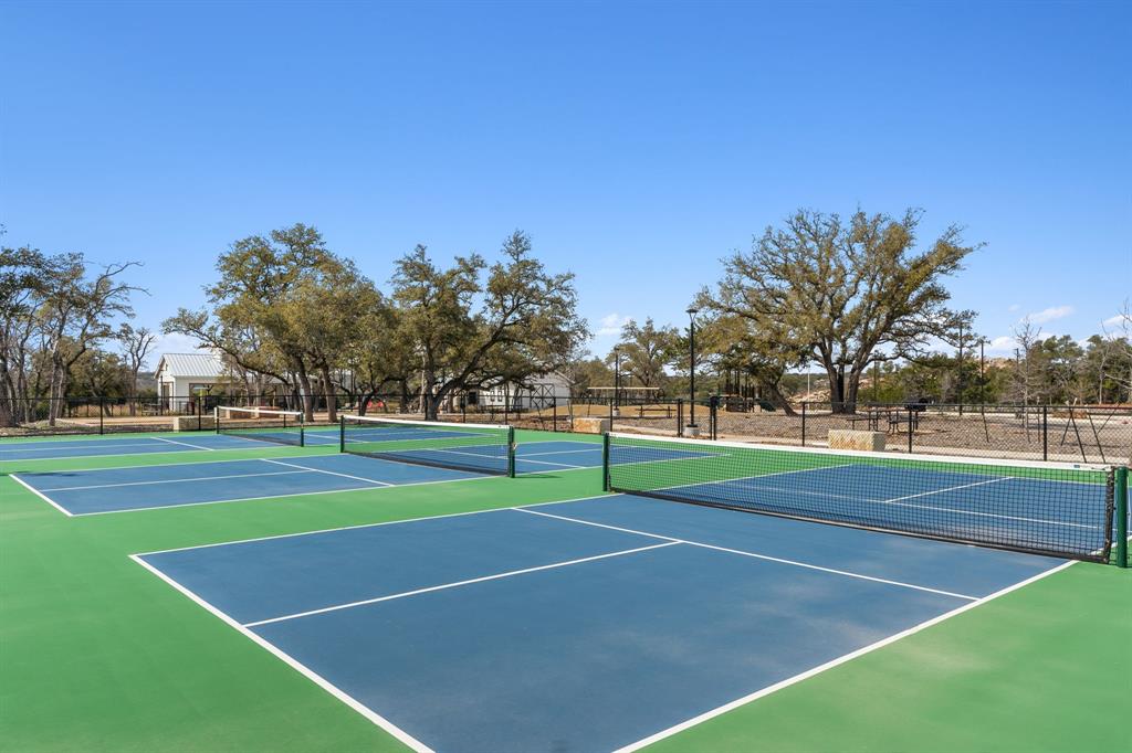 204 Swinging H Lane Georgetown, TX 78633 - Photo 34 of 39 Recreational courts featuring blue and green surfaces with white line markings and nets, surrounded by mature trees and clear skies
