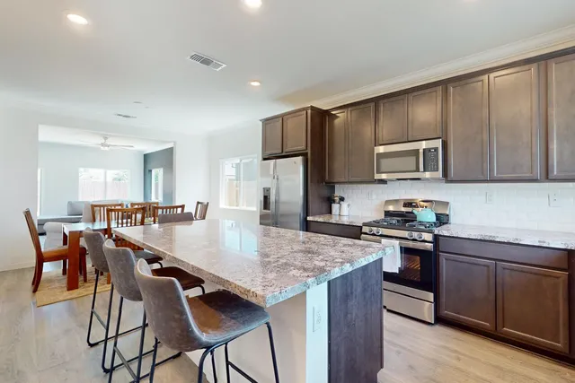 a kitchen with stainless steel appliances granite countertop a stove a sink a microwave a dining table and chairs with wooden floor