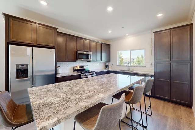 a kitchen with stainless steel appliances granite countertop a refrigerator a stove a sink a dining table and chairs with wooden floor