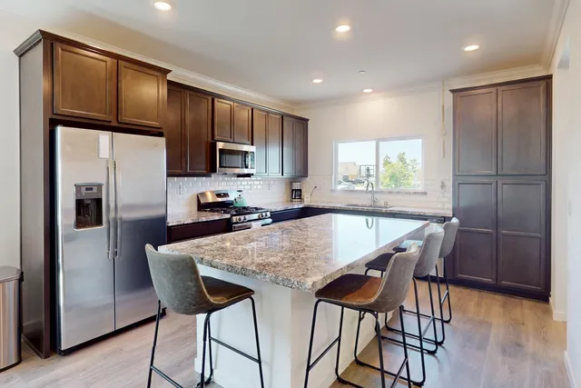 a kitchen with stainless steel appliances granite countertop a refrigerator a microwave a stove and a refrigerator with wooden floor