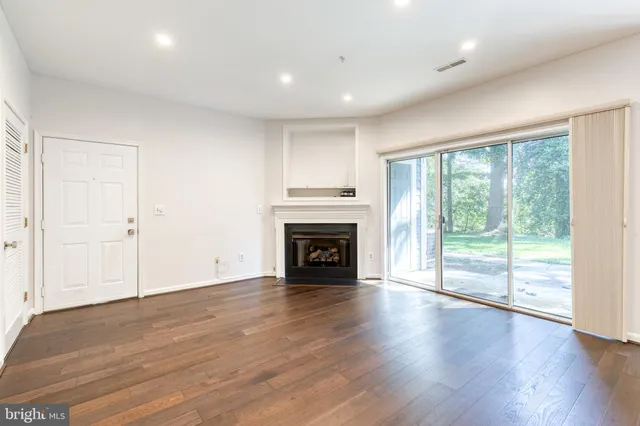 a view of an empty room with wooden floor fireplace and a window