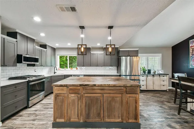 a kitchen with stainless steel appliances granite countertop a stove top oven a sink dishwasher a dining table and chairs with wooden floor