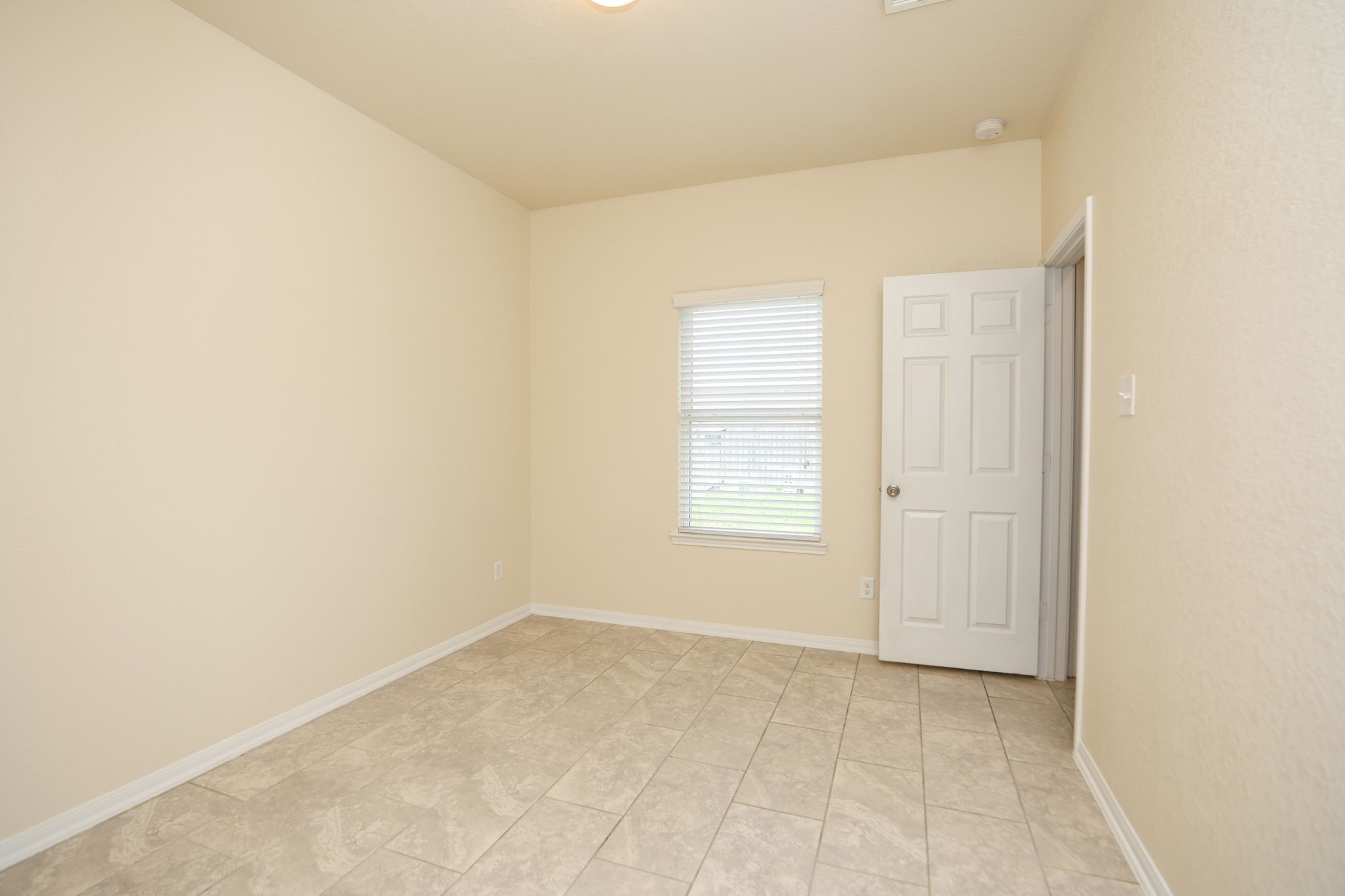 18402 Spruce Tree Line Trail Houston, TX 77084 - Photo 11 of 30 This photo shows a small, bright room with light-colored walls and tiled flooring. It features a window with blinds and a white door, ideal for use as an office or guest room.