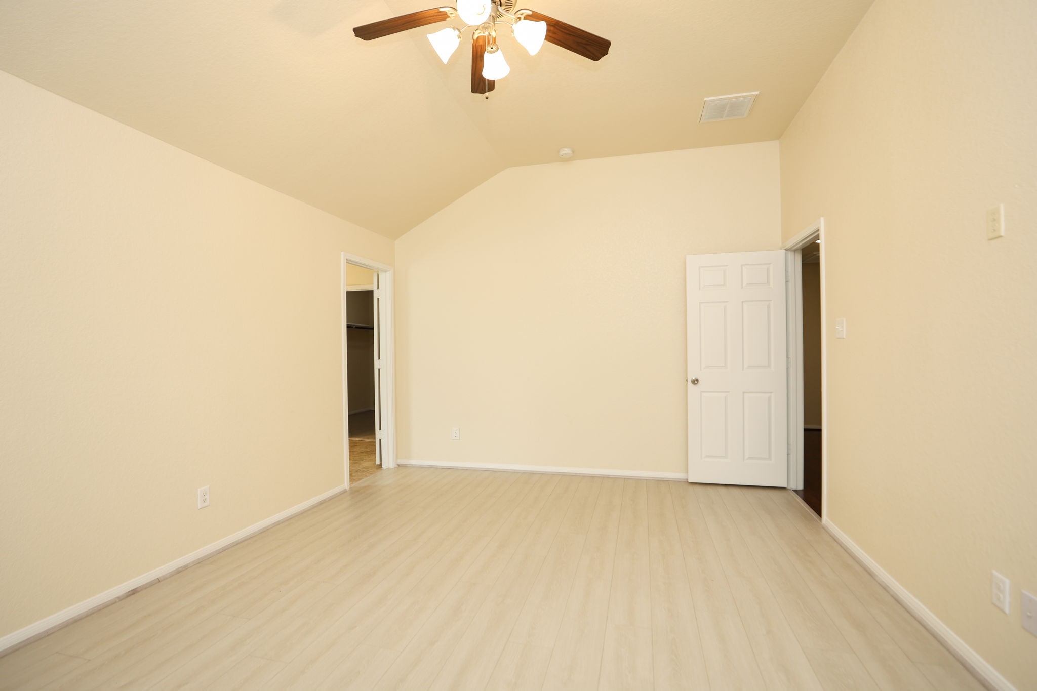 18402 Spruce Tree Line Trail Houston, TX 77084 - Photo 17 of 30 This photo shows a spacious, empty room with light-colored walls and flooring, a ceiling fan with lights, and two open doorways leading to adjacent rooms.